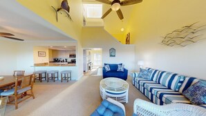 A spacious living area with a blue sofa, a dining table with chairs, a kitchen in the background, and a ceiling fan. - Lakeside Retreat in Gated Litchfield by the Sea (Pawleys Island)