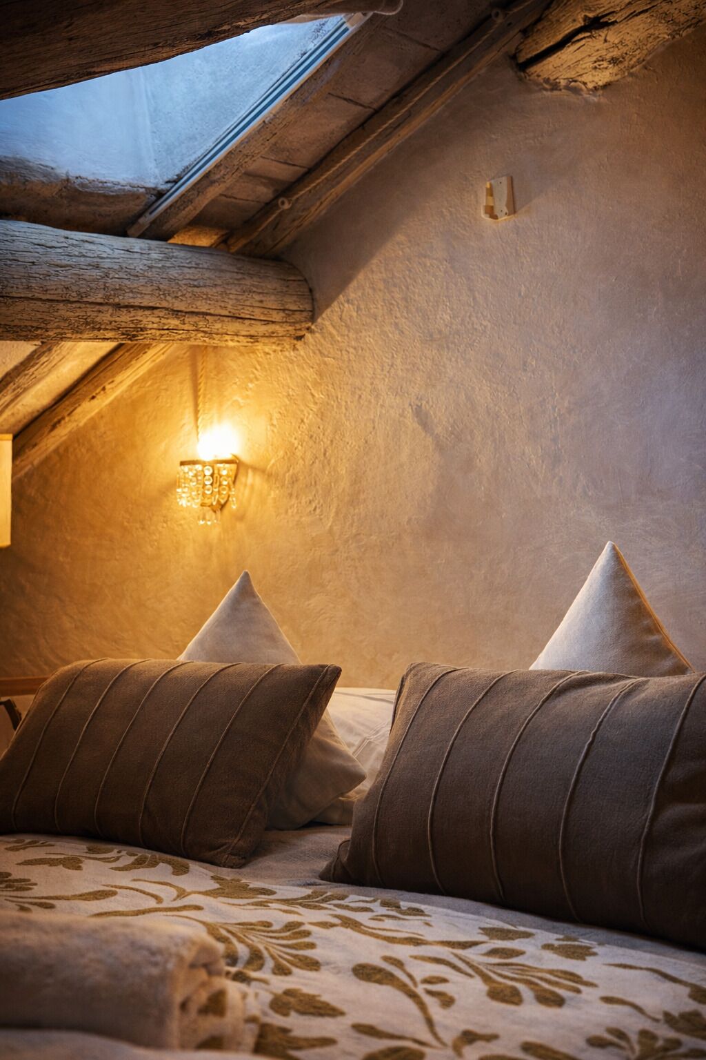 A cozy room with a sloped ceiling, a skylight, and a wall-mounted light fixture.