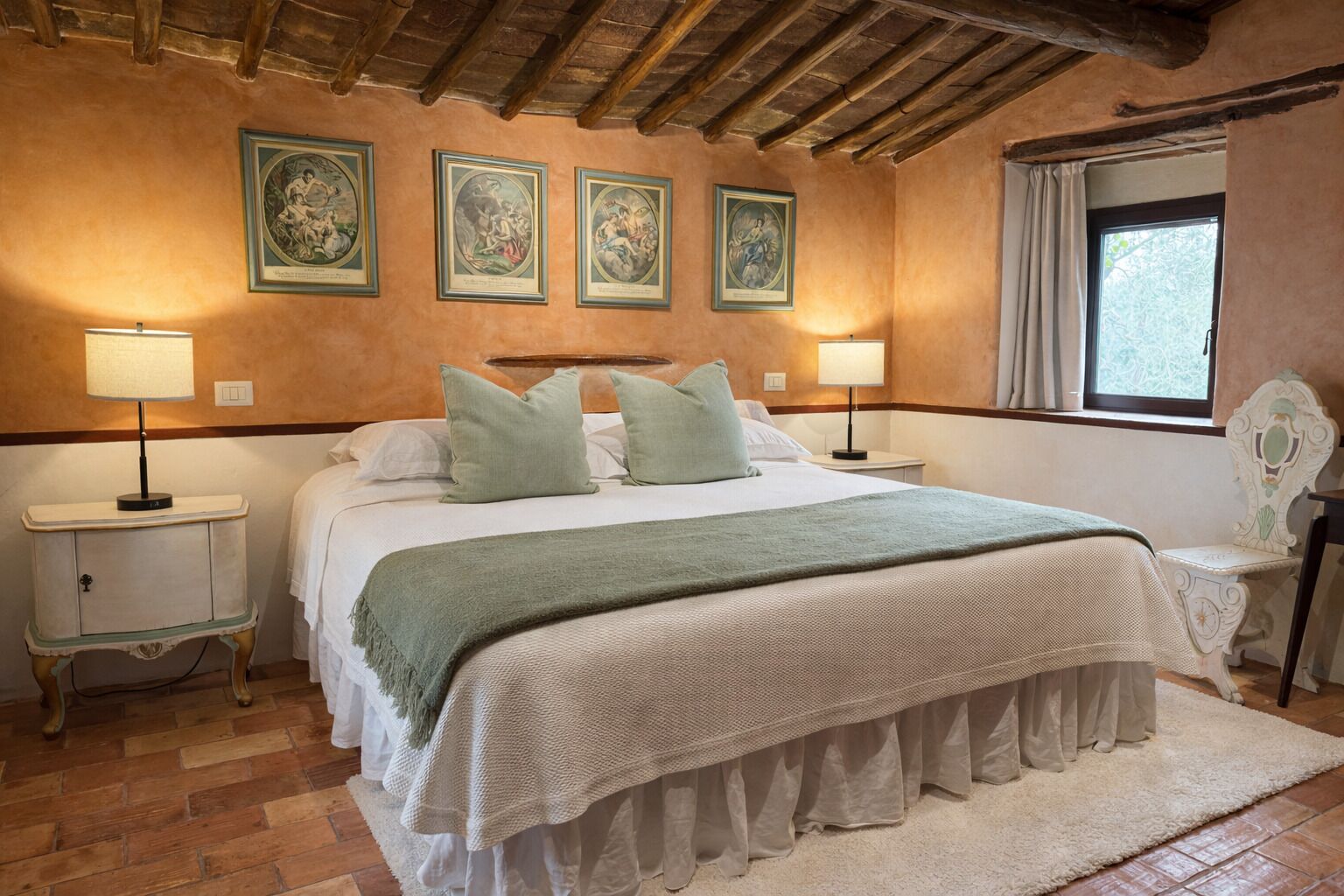 A bedroom with a large bed, two bedside tables with lamps, a window with curtains, and a wooden ceiling.