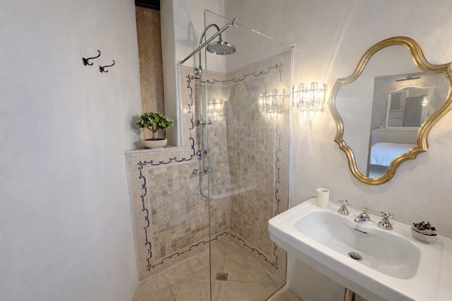 A bathroom with a glass-enclosed shower, a white sink, a gold-framed mirror, and a small potted plant.