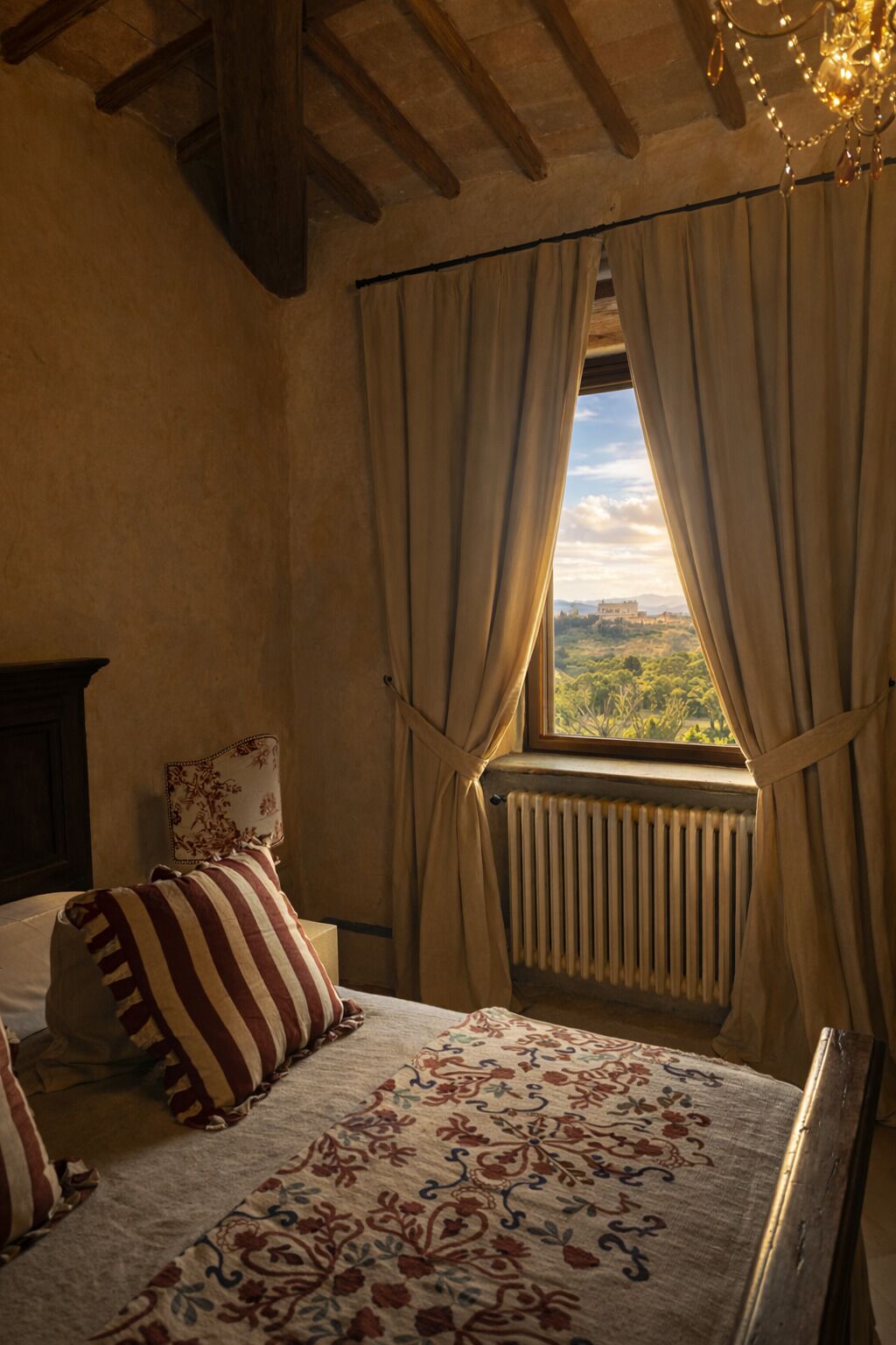Une chambre à coucher avec un lit, un radiateur, des rideaux et une vue sur la verdure à l’extérieur.