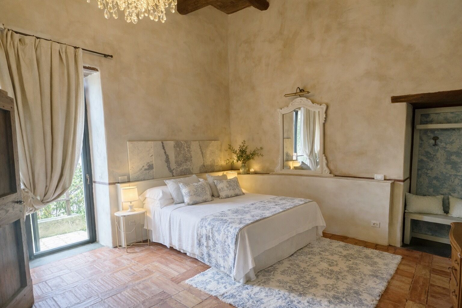 A bedroom with a bed, bedside lamps, a mirror, a window with curtains, and a wooden floor.