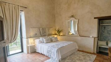 A bedroom with a bed, bedside lamps, a mirror, a window with curtains, and a wooden floor.