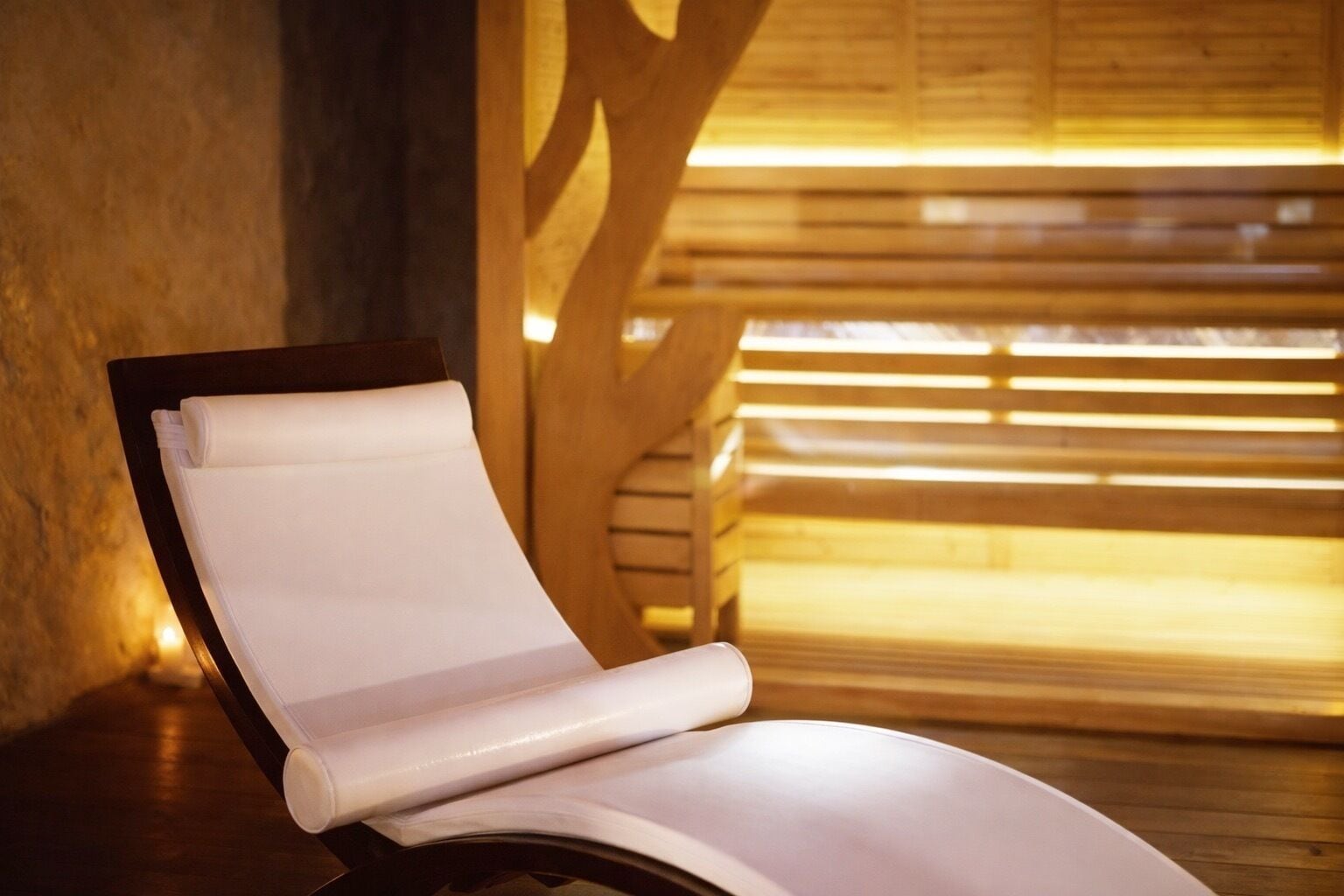 A modern lounge chair with a white cushion, positioned in a room with wooden slats and a warm light source.