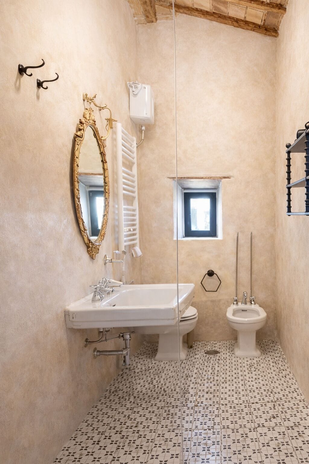 Un baño con un lavabo blanco, un espejo con marco dorado, un inodoro blanco y una ventana pequeña.