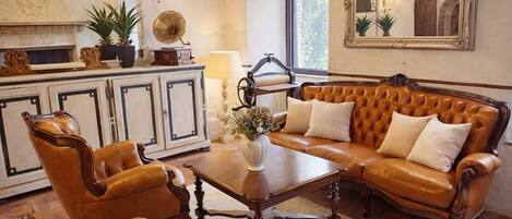A traditional living room with a leather sofa, matching armchairs, a wooden coffee table, a vintage gramophone, and a large mirror.