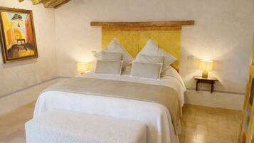 Quarto com cama, almofadas, mesa de cabeceira, luminária, quadro e teto de madeira.