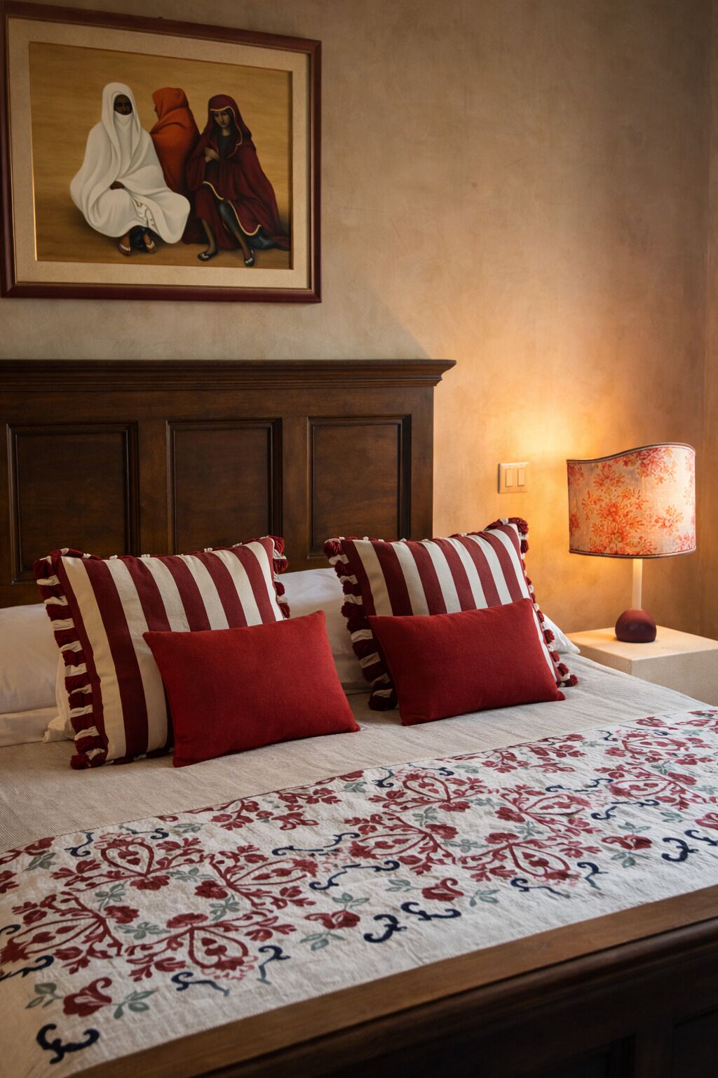 Un cuarto de hotel con una cama grande, almohadas a rayas, una colcha estampada, una mesita de noche con una lámpara y un cuadro en la pared.