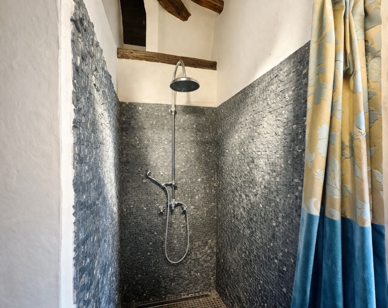 A shower with a handheld showerhead and a rain shower attachment, a tiled wall, and a blue curtain.
