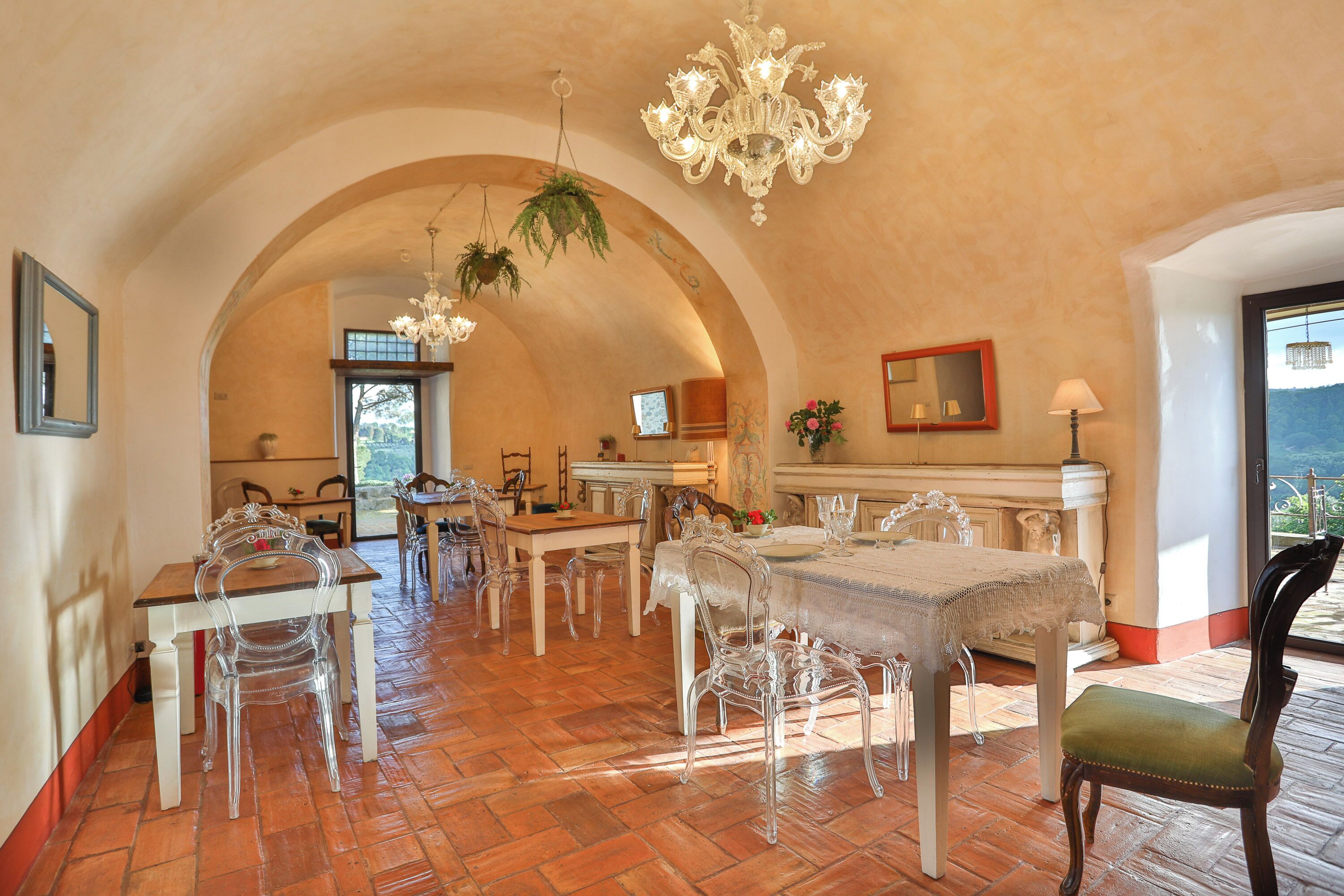 Un espace repas avec des chaises transparentes, un lustre et une vue sur l’extérieur, visible à travers une porte en arc de cercle.