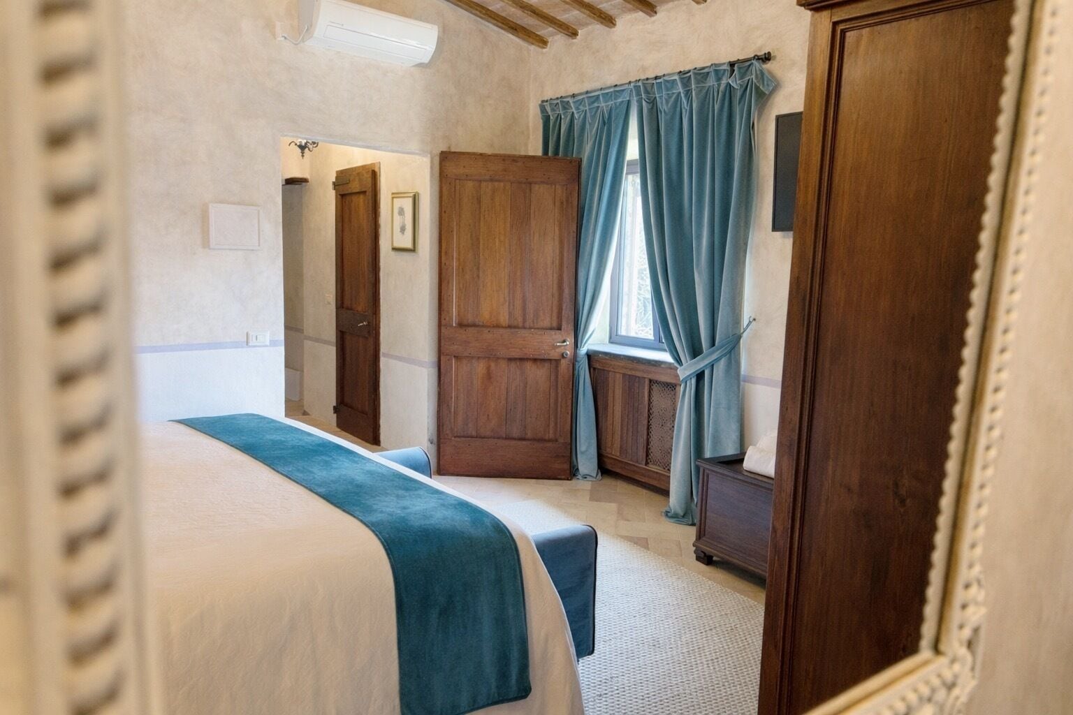 A bedroom with a bed, a wooden wardrobe, a window with curtains, and a radiator.