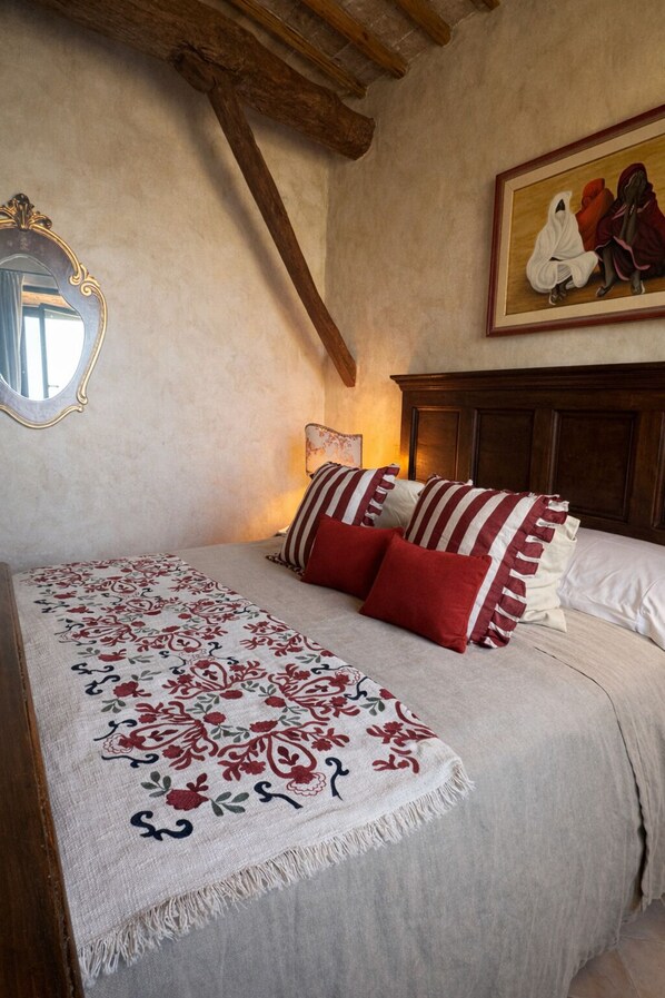 A bedroom with a bed, pillows, a bedside lamp, a mirror, and a painting on the wall. - Torre Collevento Luxury Villa (Orvieto)