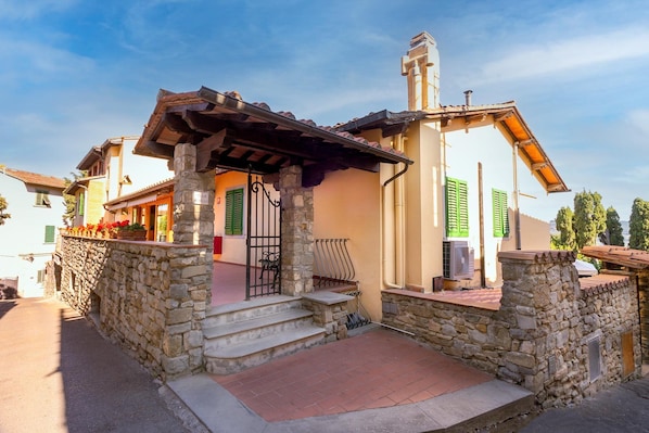 Una casa de paredes de piedra con un porche de madera, contraventanas verdes y una chimenea.