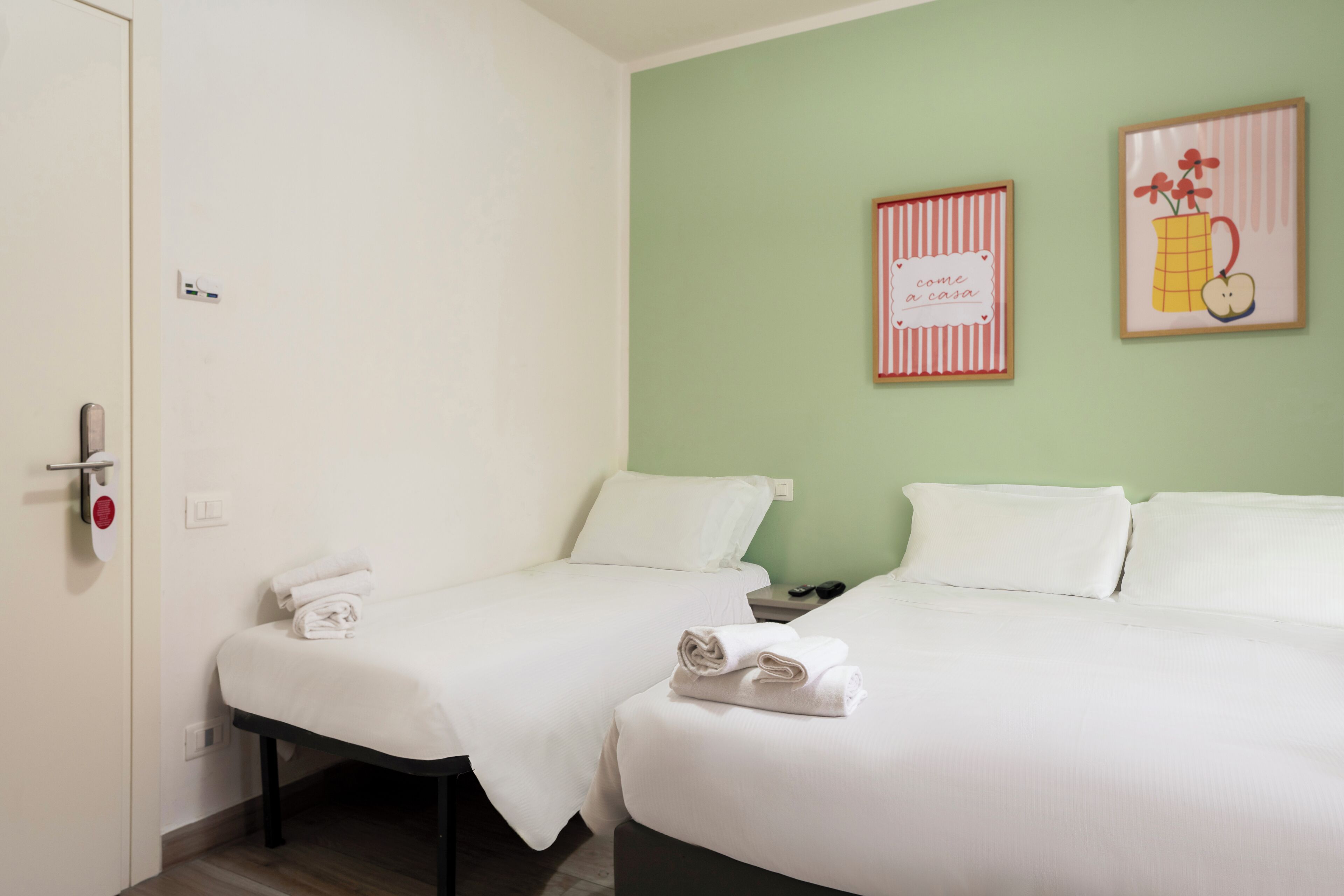 Een hotelkamer met twee bedden, wit beddengoed, een groene muur en twee ingelijste foto's.