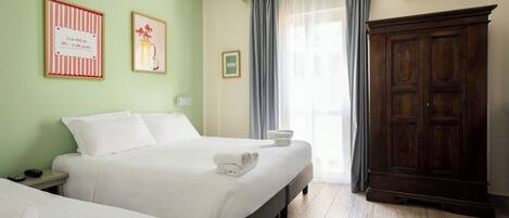 A hotel room with two beds, a wardrobe, and a window with curtains.