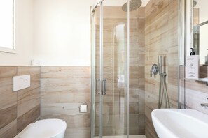 Un baño moderno con ducha de vidrio, inodoro y lavamanos con dispensador de jabón.