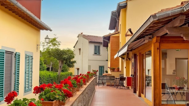 A narrow street with buildings on either side, a stone wall with potted plants, and a clear sky. - Hotel Villa Bonelli (Fiesole)