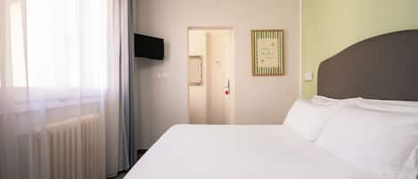 A hotel room with a bed, a television, a door, and a wall with a framed sign.