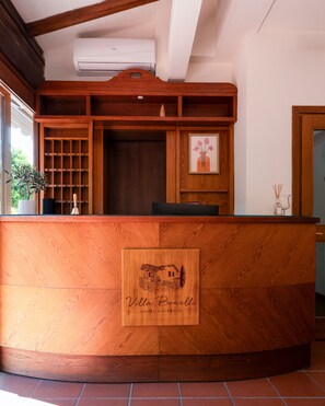 Un mostrador de recepción con detalles de madera, una obra de arte enmarcada encima y una planta en maceta a la izquierda.