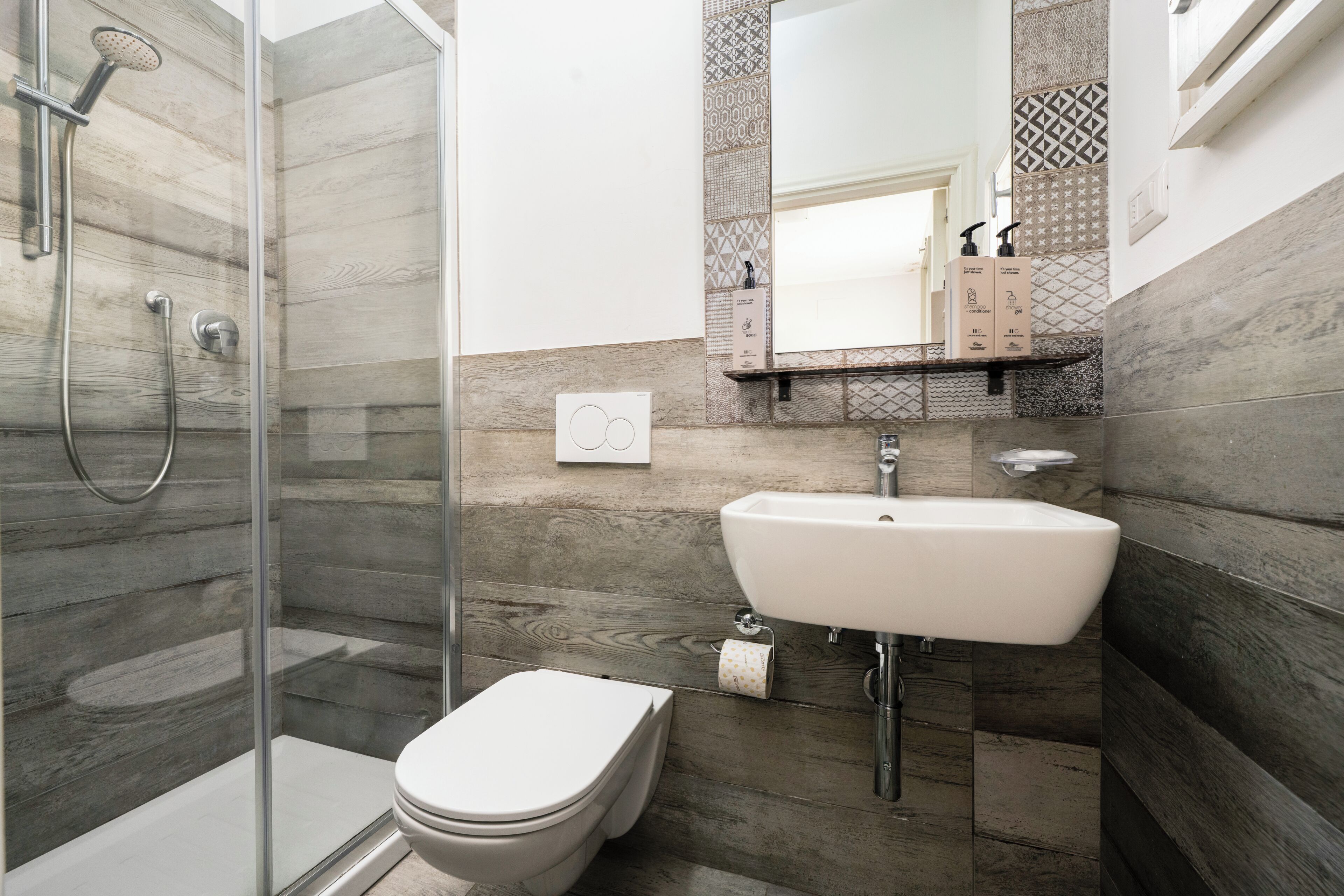 A modern bathroom with a glass-enclosed shower, a white toilet, and a sink with a mirror above.