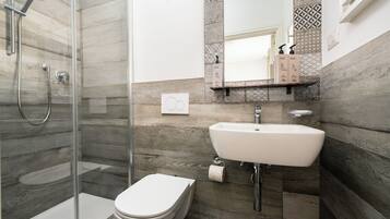 A modern bathroom with a glass-enclosed shower, a white toilet, and a sink with a mirror above.