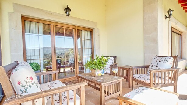 A sunlit patio with wooden furniture, large windows, and potted plants. - Home in Comillas · 3 bedrooms · 4 beds · 3 baths (Ruiloba)