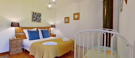 A bedroom with a bed, bedside tables, a crib, and hanging light fixtures.