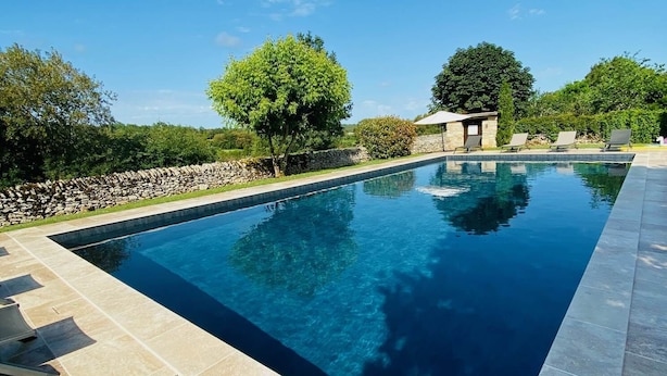 A rectangular swimming pool with a stone border, surrounded by a stone wall and trees.