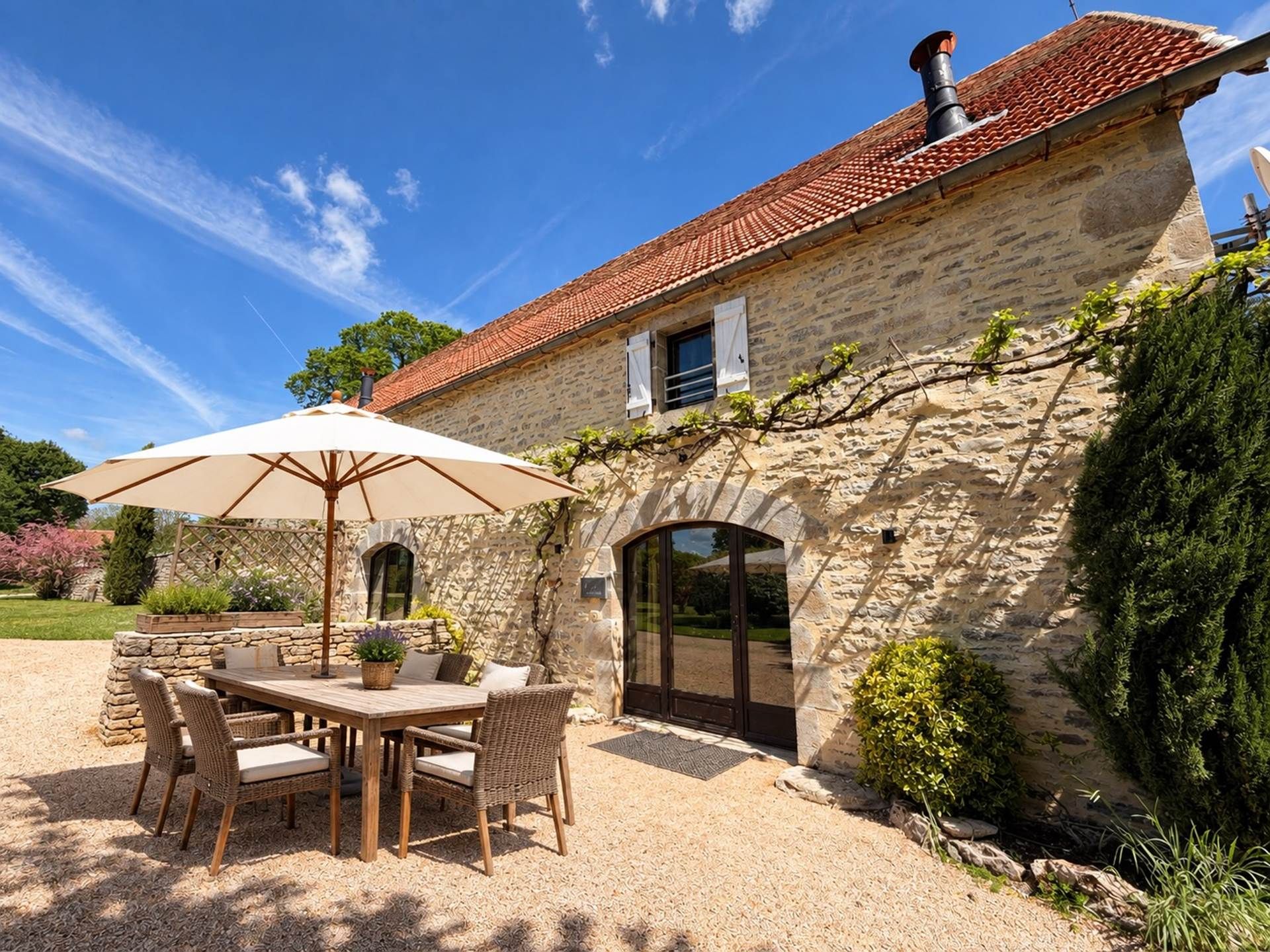A stone house with a tiled roof, a patio with a table and chairs, and a large umbrella.
