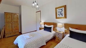 A bedroom with two beds, wooden wardrobe, bedside tables with lamps, and a mirror.