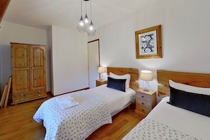 Une chambre avec deux lits, une armoire en bois, des tables de chevet avec des lampes et un miroir.