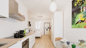Una cocina moderna con encimera de madera, microondas y hervidor. Hay un comedor con mesa y sillas de vidrio.
