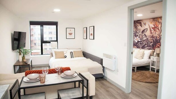 A modern hotel room with a bed, a dining area, and a view of the city. - City Centre Apartment, Quiet and Cozy, Sleeps 4. (Liverpool)