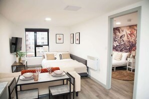 A modern hotel room with a bed, a dining area, and a view of the city. - City Centre Apartment, Quiet and Cozy, Sleeps 4. (Liverpool)