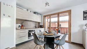 A modern kitchen with white cabinets, a built-in oven, and a dining area with a round table and chairs. - Ambre blanche - Les Gets - Centre village (Les Gets)