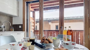 A breakfast table with croissants, coffee, and juice, set in a modern kitchen with large windows. - Ambre blanche - Les Gets - Centre village (Les Gets)
