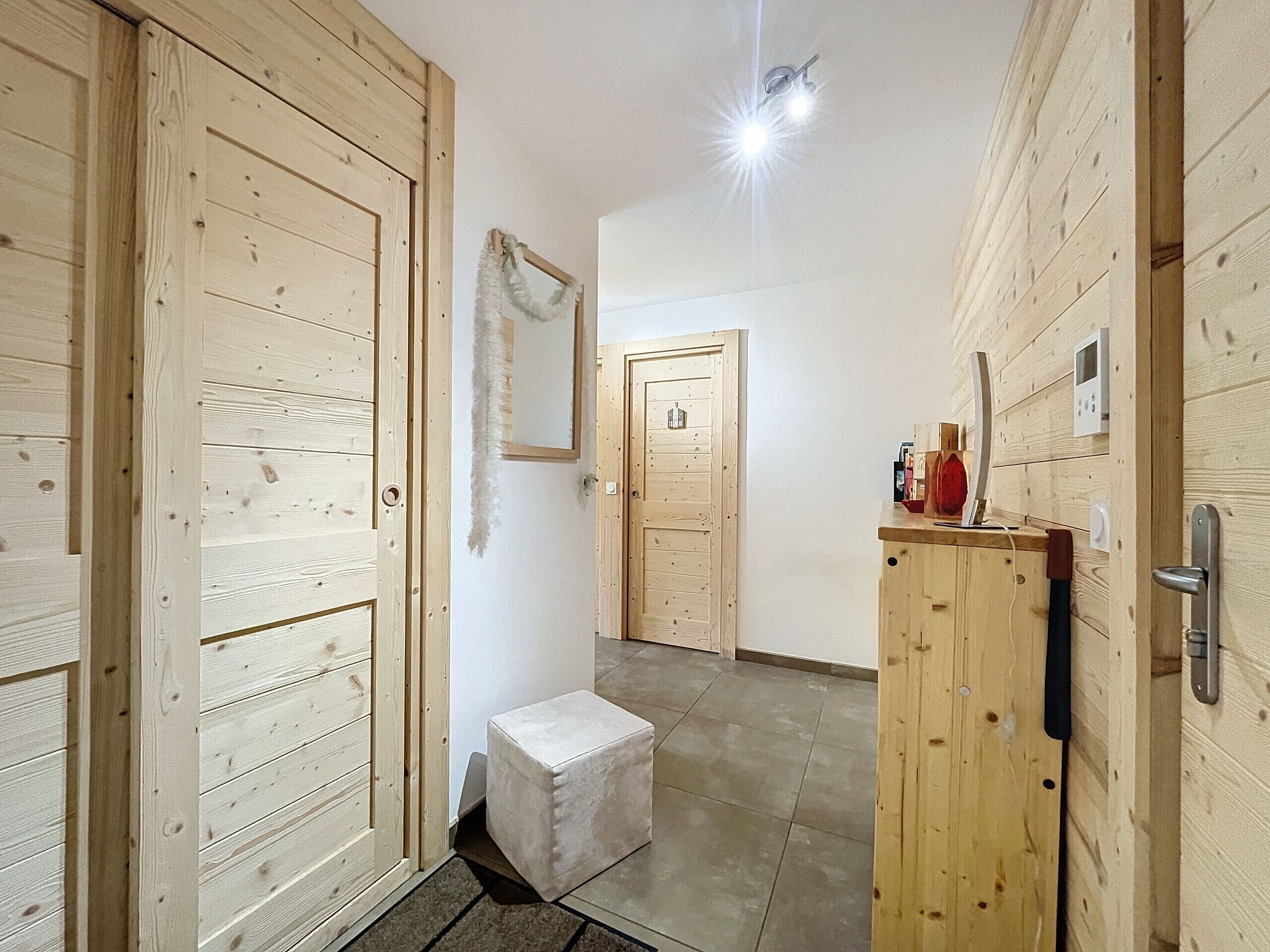 A hallway with wooden doors, a small white bench, and a wooden cabinet with a handle.