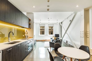 A modern kitchen with dark cabinetry, a white countertop, and a dining area with a round table and chairs.