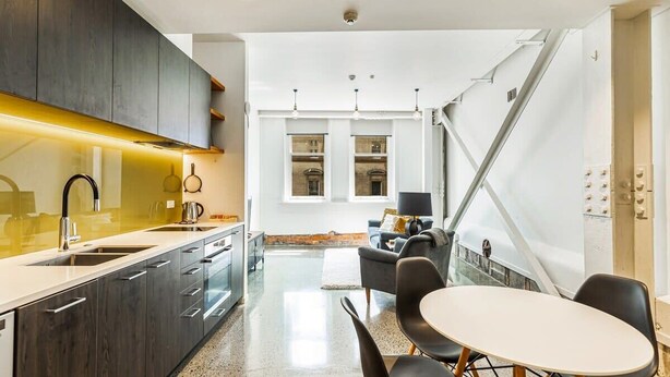 Una cocina moderna con armarios oscuros, una encimera blanca y una zona de comedor con mesa y sillas.
