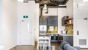 Ein modernes Interieur mit einer Küchenzeile, einem Essbereich mit Tisch und Stühlen, einer Couch und einer weißen Tür mit Notausgangsschild.