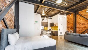 Ein modernes Hotelzimmer mit Bett, Sofa, einer Küchenzeile und einer Wand mit freiliegenden Backsteinen.