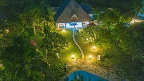 Vista aérea de una casa con techo de paja, rodeada de exuberante vegetación y una piscina.