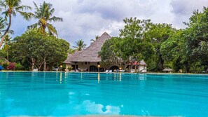 A swimming pool with a thatched-roof building in the background, surrounded by lush greenery.