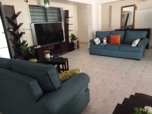 A living room with a large flat-screen TV, a blue sofa, and a staircase leading to another room.
