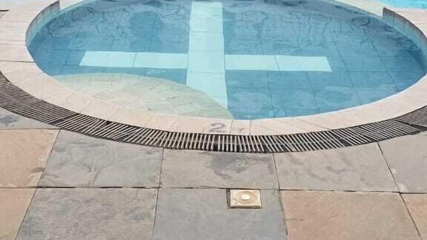 A swimming pool with a tiled deck and a small hot tub in the center.