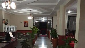A hotel lobby with a checkered floor, a reception desk, potted plants, and a chandelier.