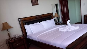 A neatly made bed with white linens and a towel shaped like a swan, a wooden nightstand with a lamp, and a mirror on the wall.