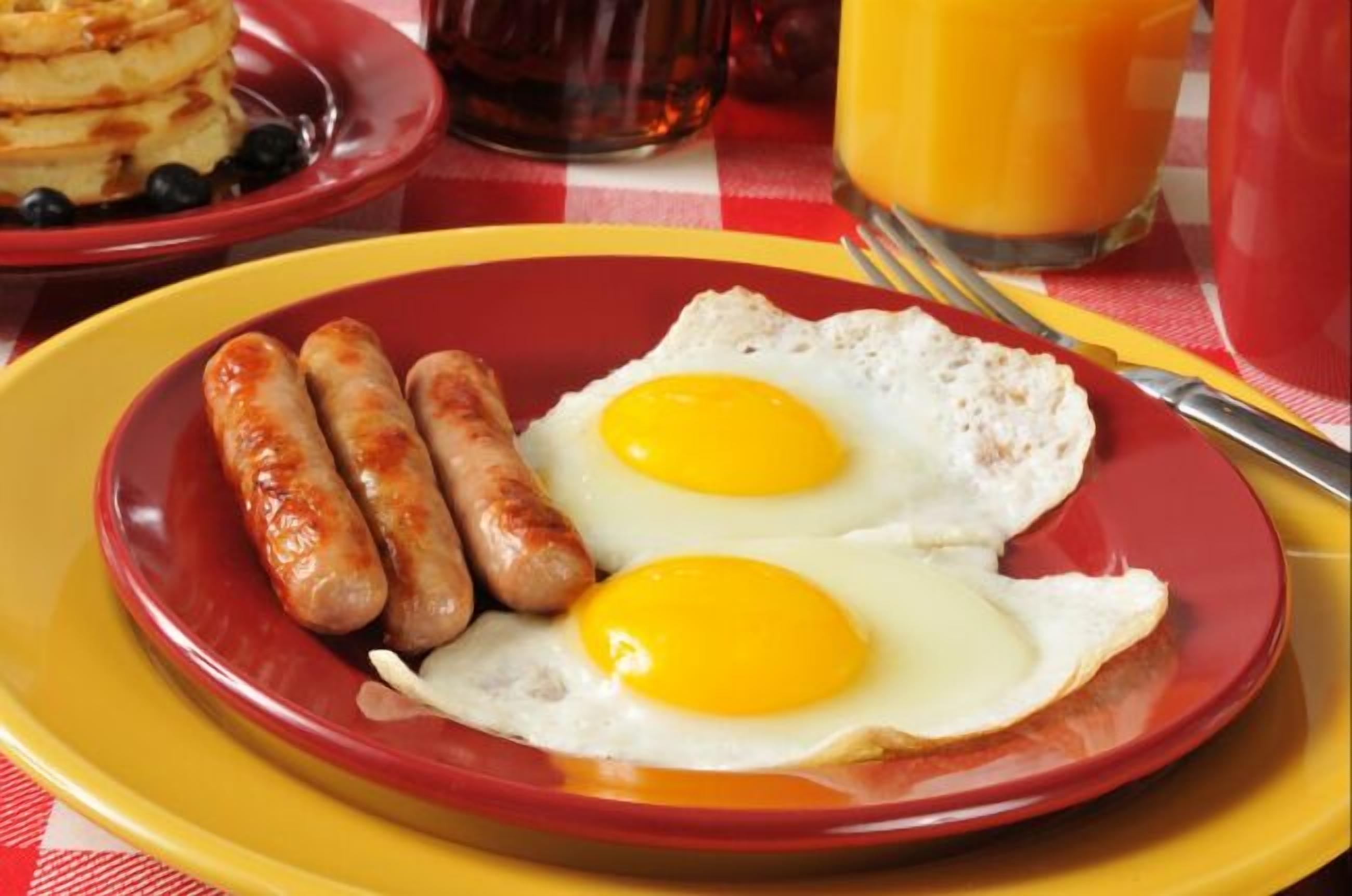 Une assiette de petit-déjeuner avec deux œufs au plat et des saucisses, le tout servi sur une assiette rouge.