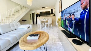Una sala de estar moderna con un sofá blanco, una mesa de centro de madera y un televisor de pantalla plana grande.