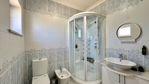 Badeværelse med glasvæg omkring bruseniche, toilet, bidet og håndvask med spejl.